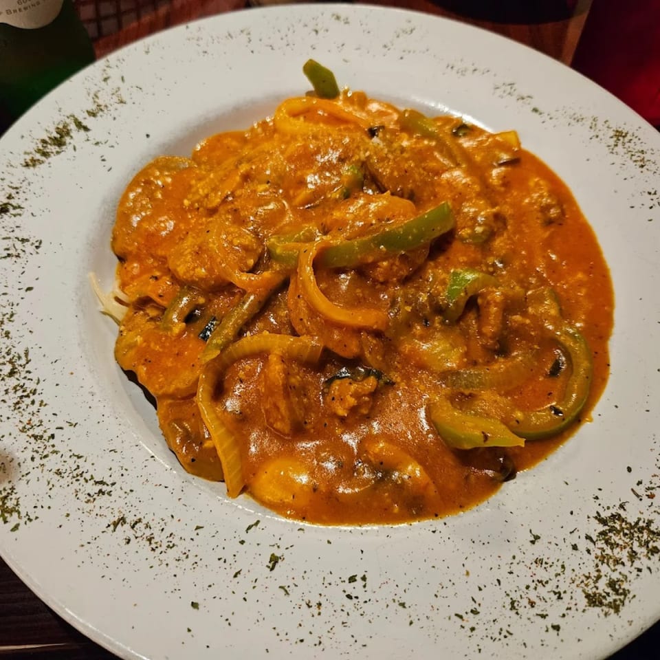 A white plate holds pasta with a rich orange sauce, green bell peppers, and onions, garnished with herbs.