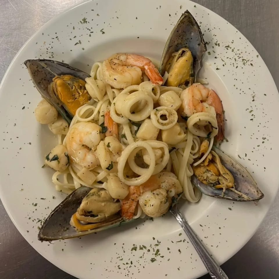 Seafood linguine with mussels, shrimp, scallops, and calamari, garnished with herbs on a white plate.
