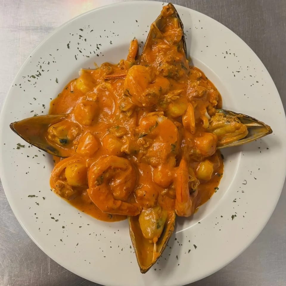 Seafood pasta with mussels and shrimp in a creamy orange sauce, garnished with herbs on a white plate.