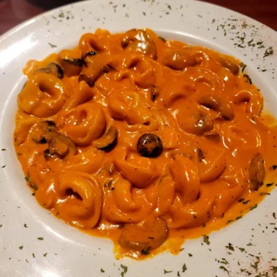 Tortellini pasta in a creamy orange sauce with mushrooms and herbs on a white plate.