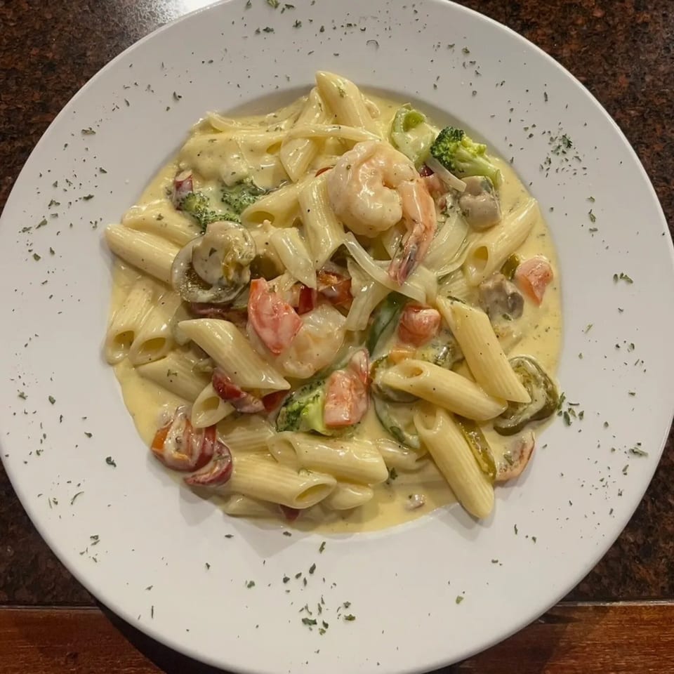 Creamy penne pasta with shrimp, broccoli, mushrooms, and tomatoes on a white plate.