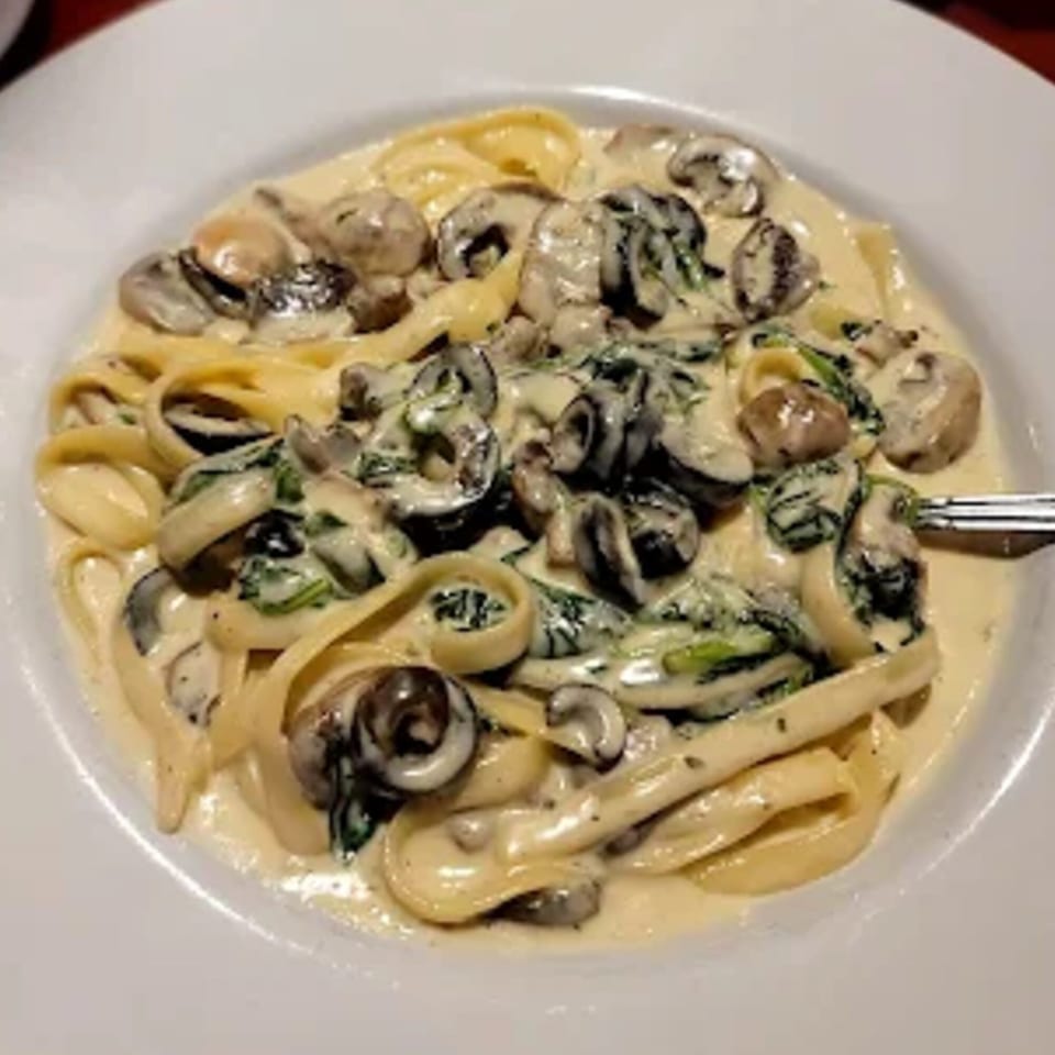 Creamy fettuccine pasta with mushrooms, spinach, and black olives in a white bowl.