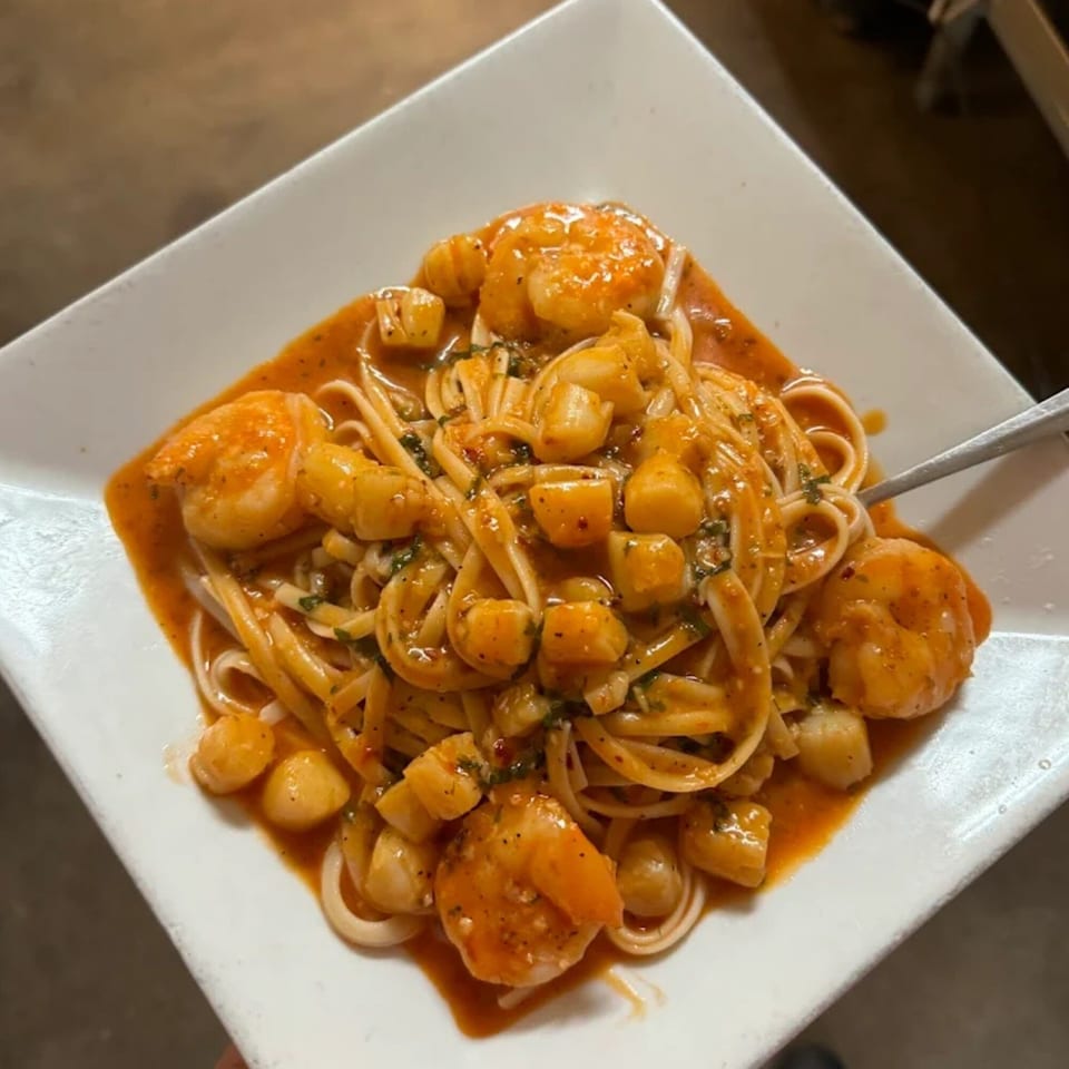 Linguine pasta with shrimp and scallops in a rich red sauce, garnished with herbs.
