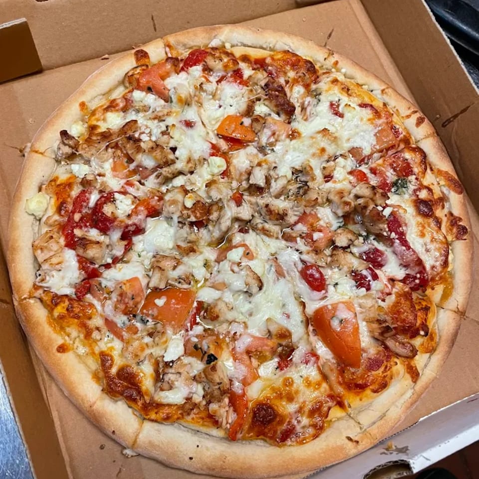 A whole pizza with chicken, tomatoes, and cheese in a cardboard delivery box.