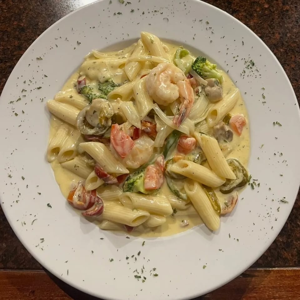 Creamy penne pasta with shrimp, broccoli, mushrooms, and tomatoes on a white plate.