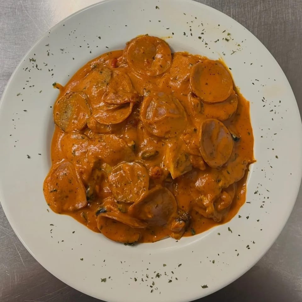 Round pasta in a creamy orange sauce, garnished with herbs on a white plate.
