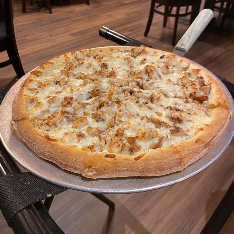 A whole chicken alfredo pizza with a golden crust on a metal tray with a pizza cutter.